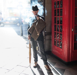 artistic photo of mature man smoking a cigar next to London phone box in tailored suit