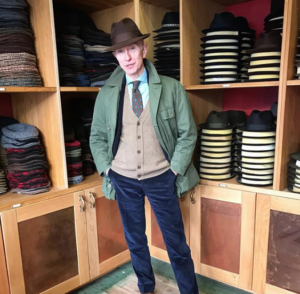 stylish mature man trying on different hats in hat shop