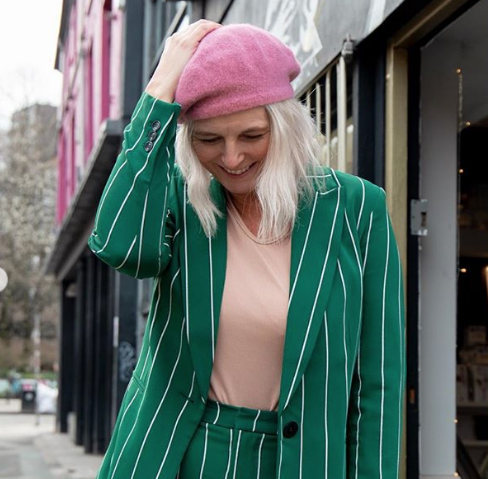 stylish middle aged woman in green striped blazer and pink hat