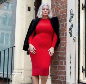 fashion forward middle aged woman leaning on street corner in a red dress
