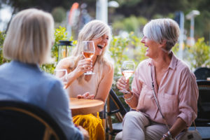 bright photo of three women at lunch together laughing and drinking wine