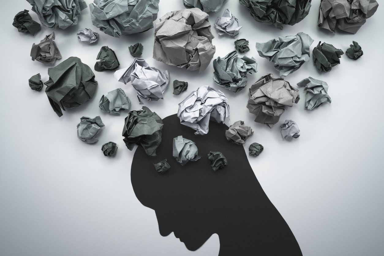 Silhouette of an anxious persons head with waste paper moving around their brain