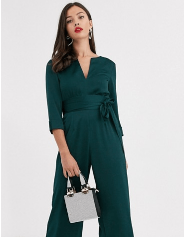 woman in an emerald jumpsuit holding a small bag