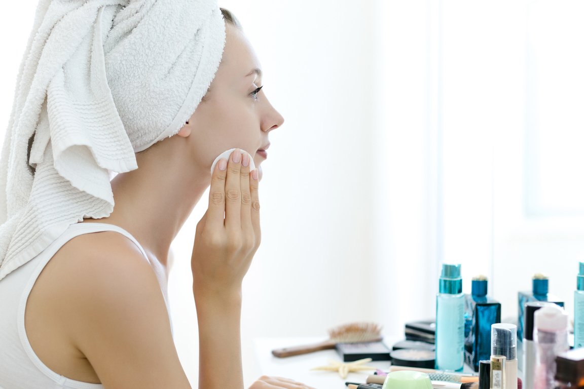 side profile of woman cleansing her face with her hair wrapped in a towel