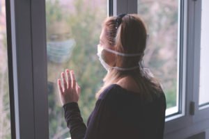 back of a woman head looking out of a window wearing a face mask