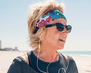 middle aged woman looking down the beach with sunglasses and bandana on