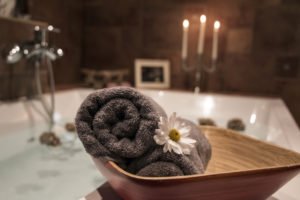bath with candles, flowers and rolled up towels, spa setting
