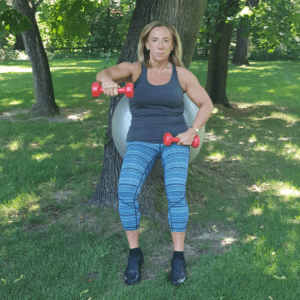 middle aged woman doing an exercise outside with an exercise ball and weights