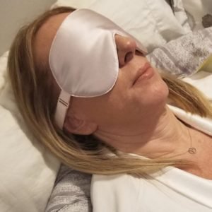 middle aged woman relaxing with eye mask on in bed